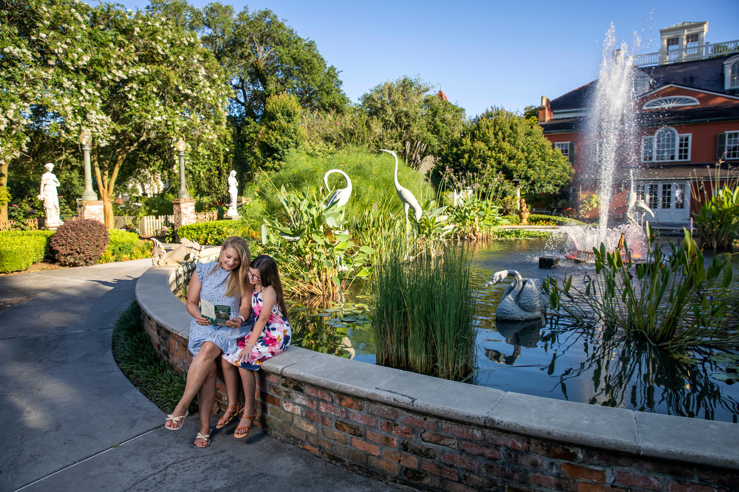 Mother and daughter sitting beside a pond at a landscaped plaza outside Houmas House Estate and Gardens in Ascension Parish, Louisiana.